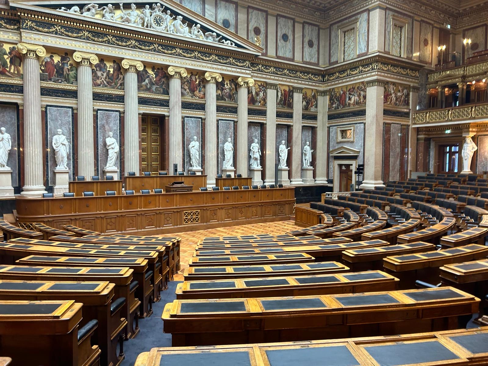 Eine Gruppe von Schülerinnen und Schülern steht bei strahlendem Sonnenschein vor dem Parlament in Wien