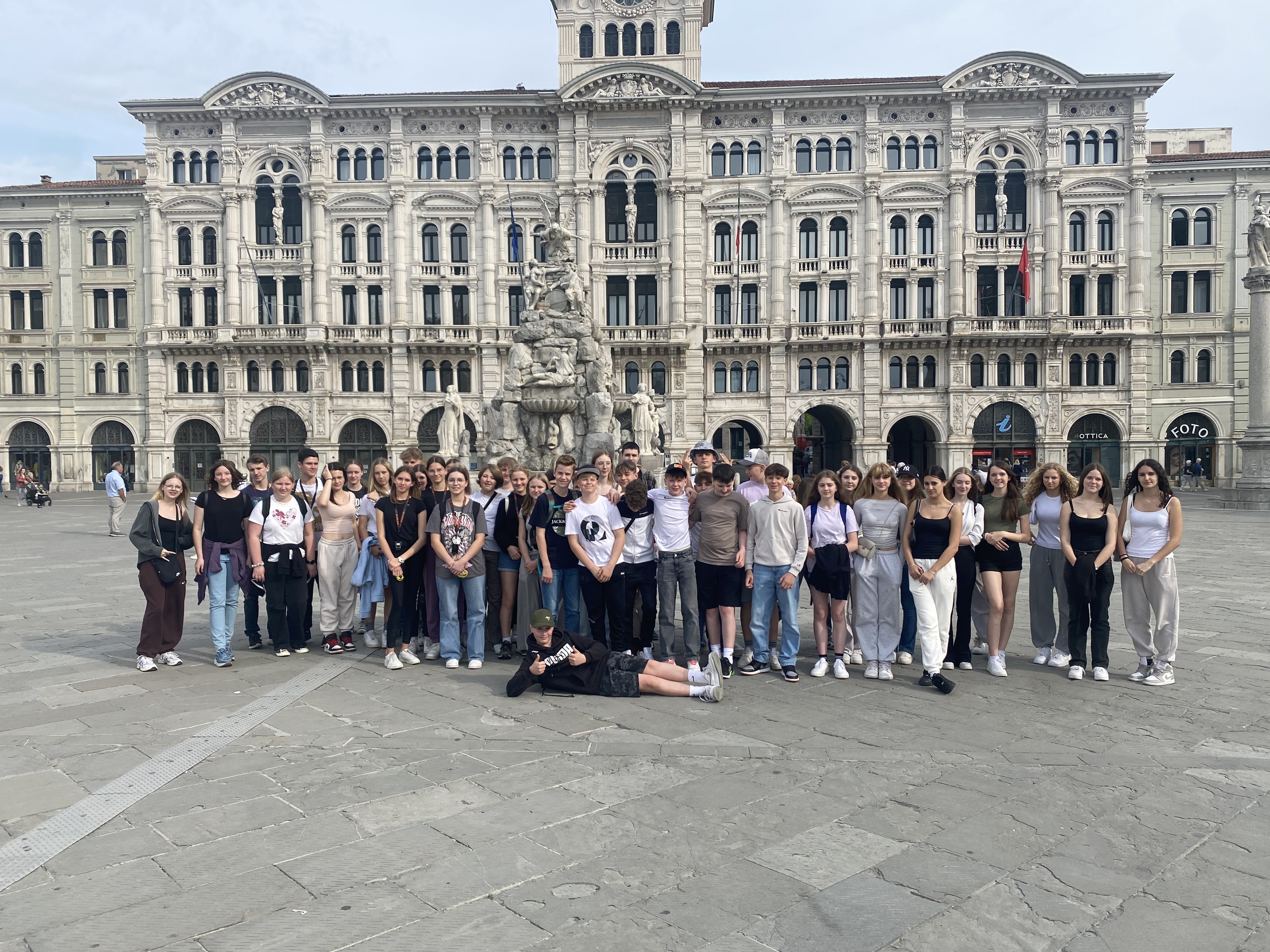 Eine Gruppe Schüler und Schülerinnen steht mit ihren Lehrer:innen vor einem imposanten Gebäude in Triest