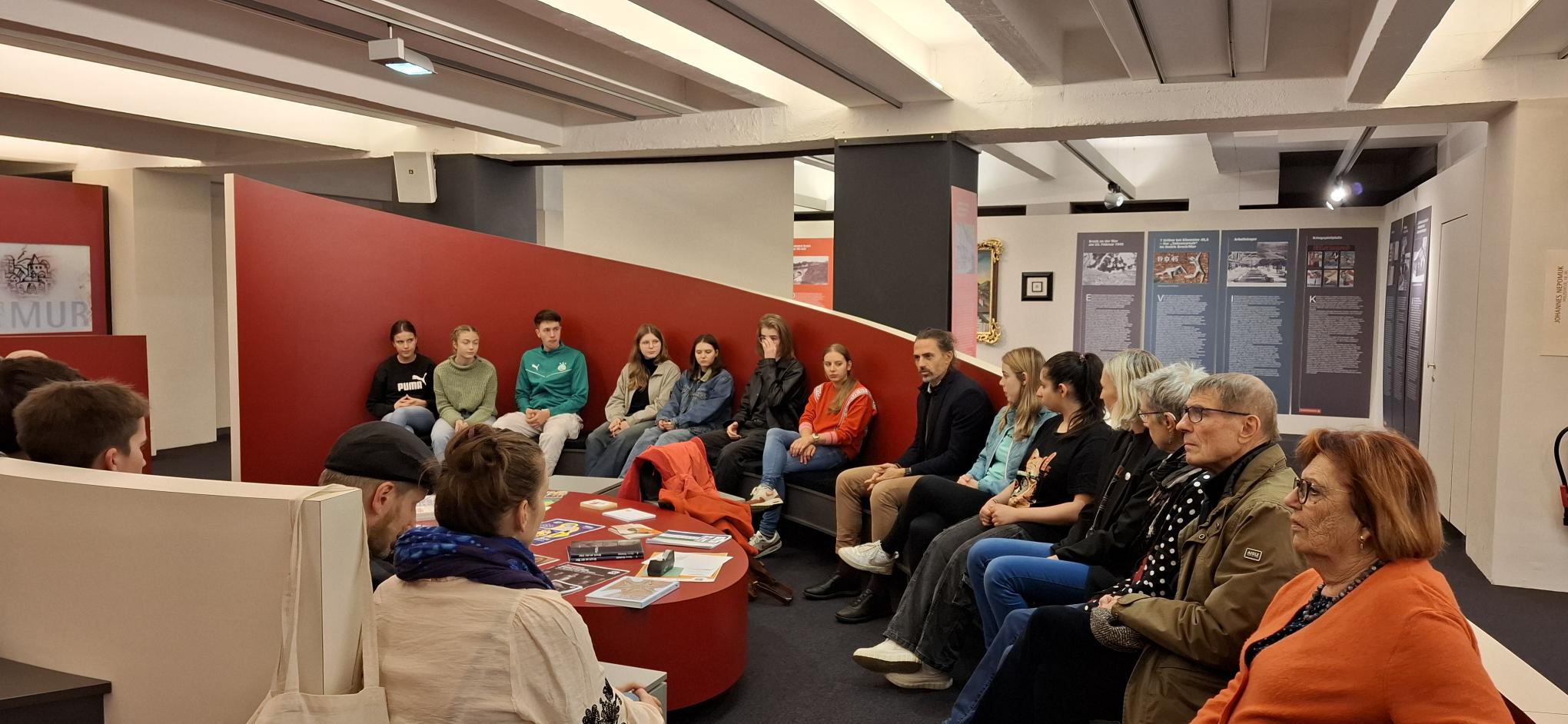 Eine Gruppe Menschen sitzt im Brucker Stadtmuseum zusammen 