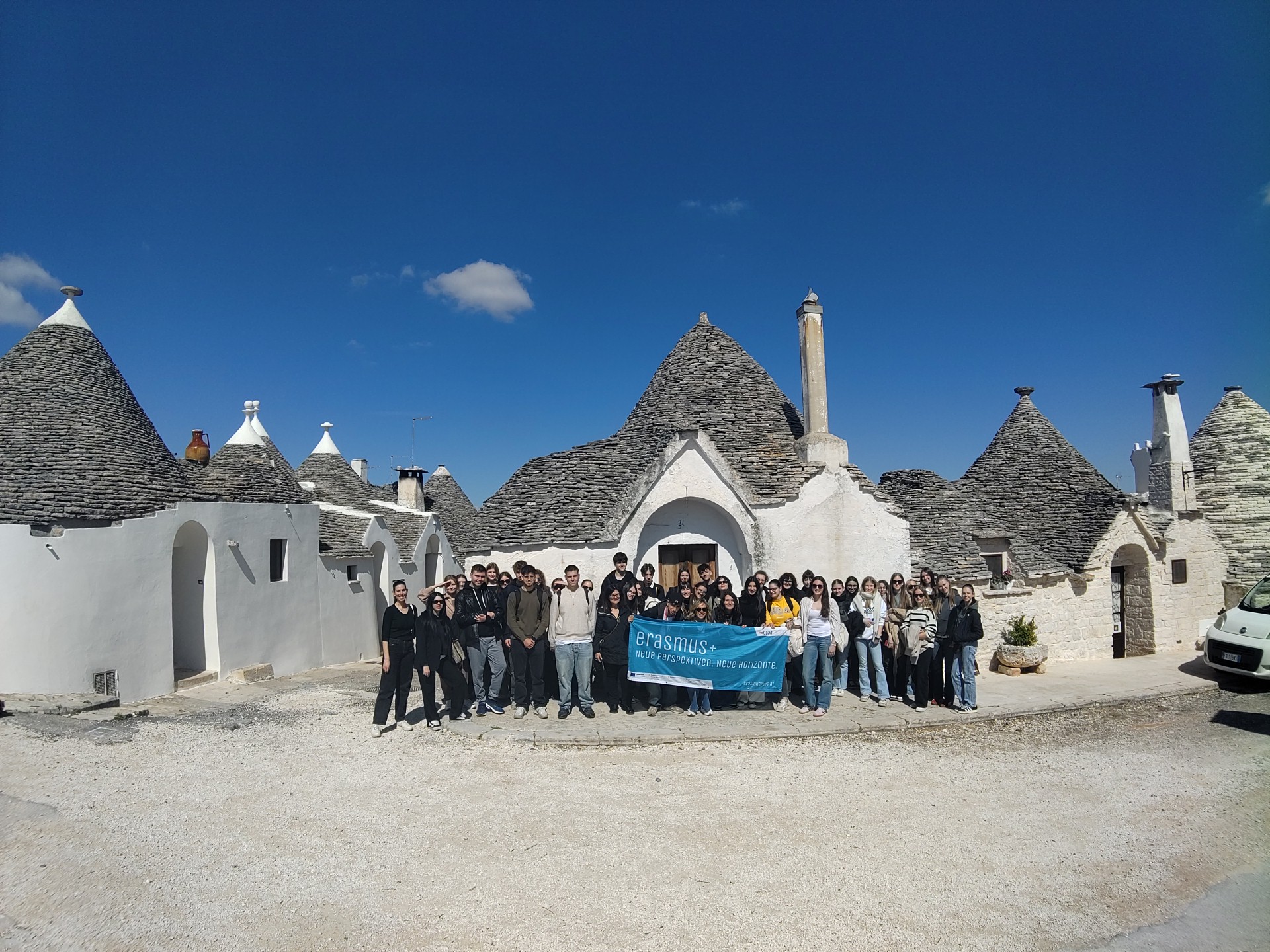 Schülergruppe mit Erasmusfahne vor einem Trulli 